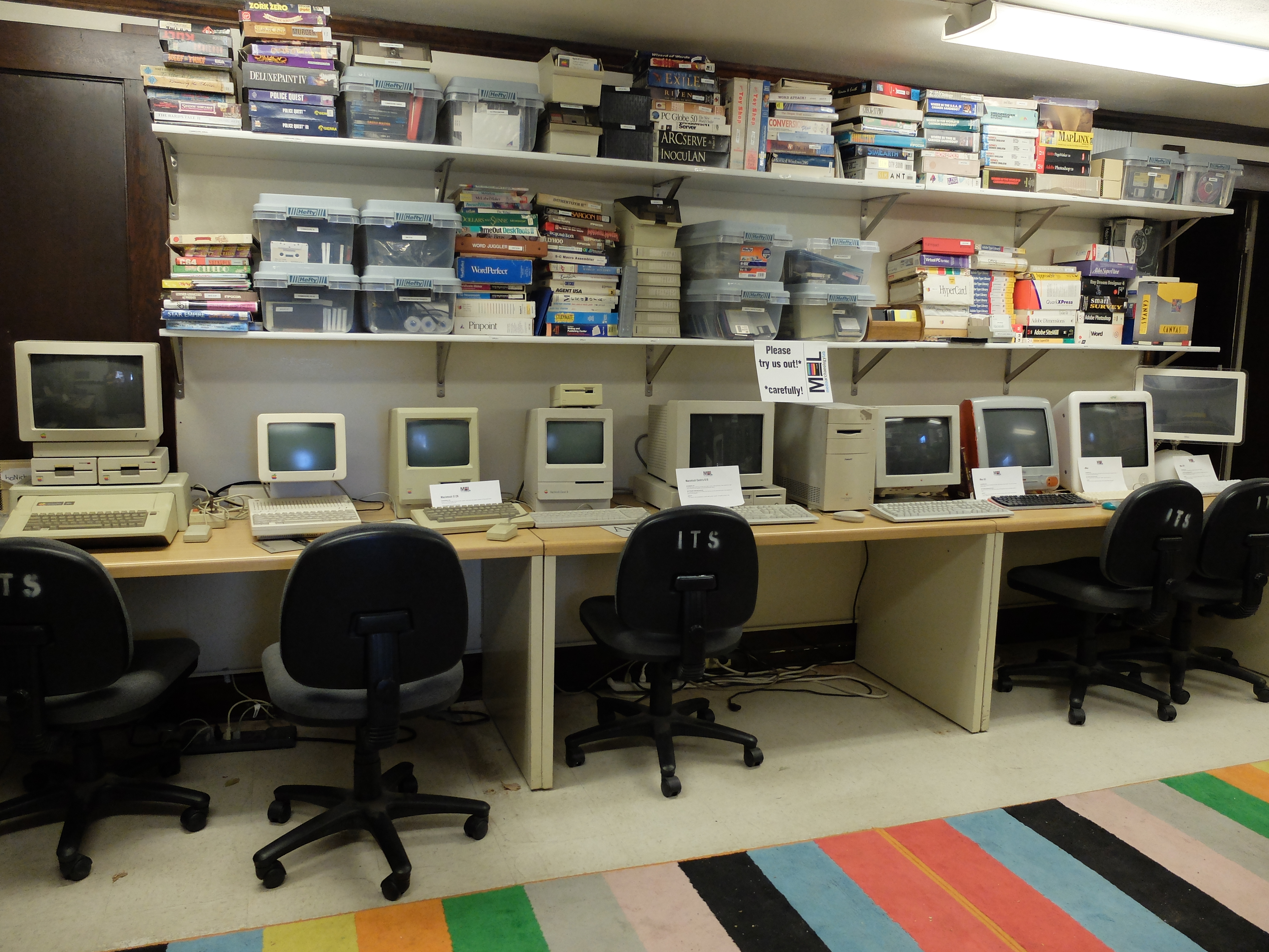 Several historic personal computers lined up on desks with a sign saying "Please try us out, carefully!"